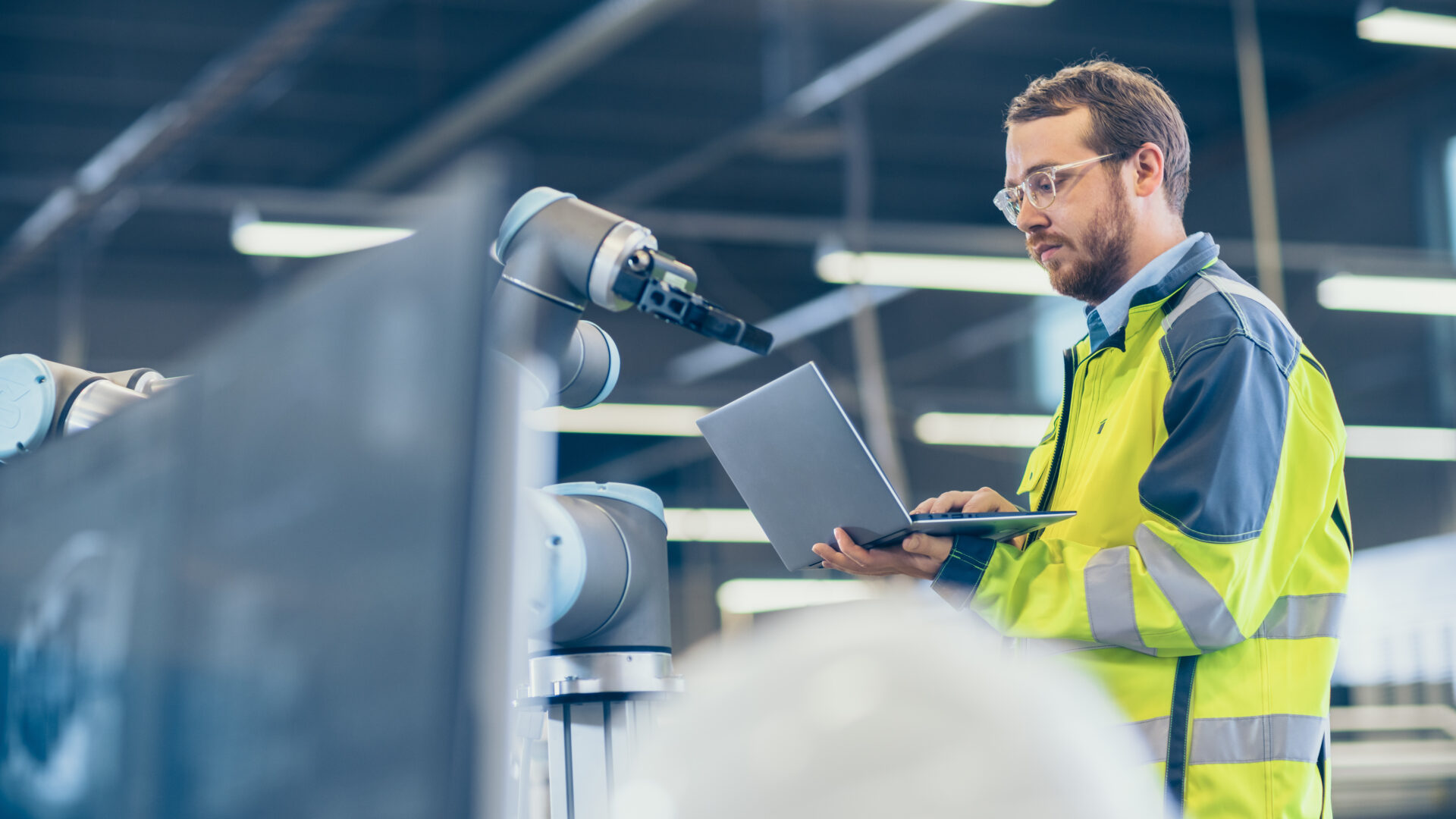 An automation engineer holding a laptop to program a robot. 