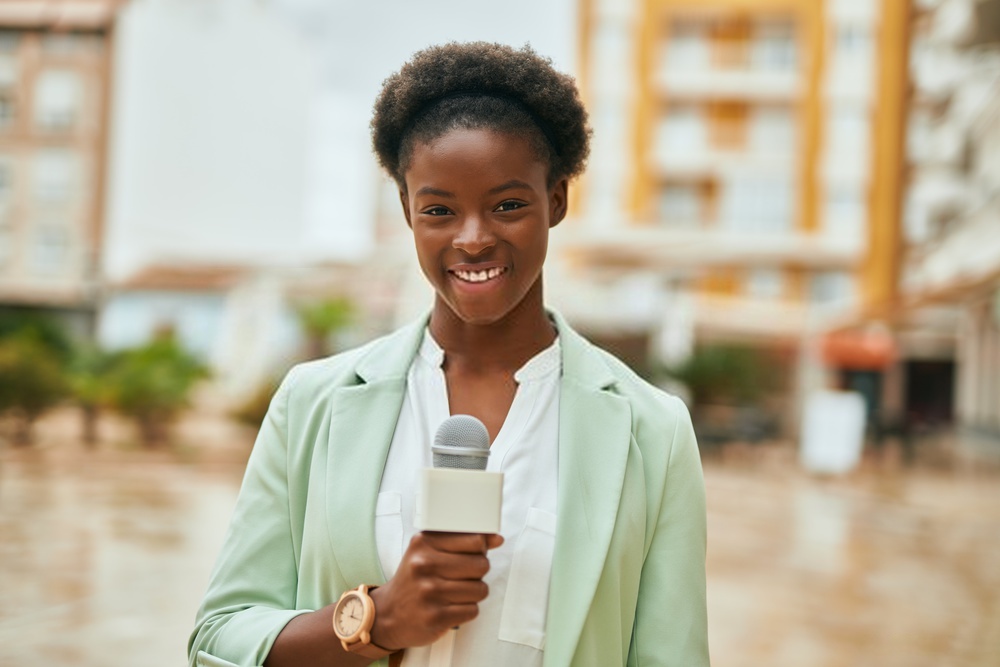 A smiling female reporter with a microphone in her hand.