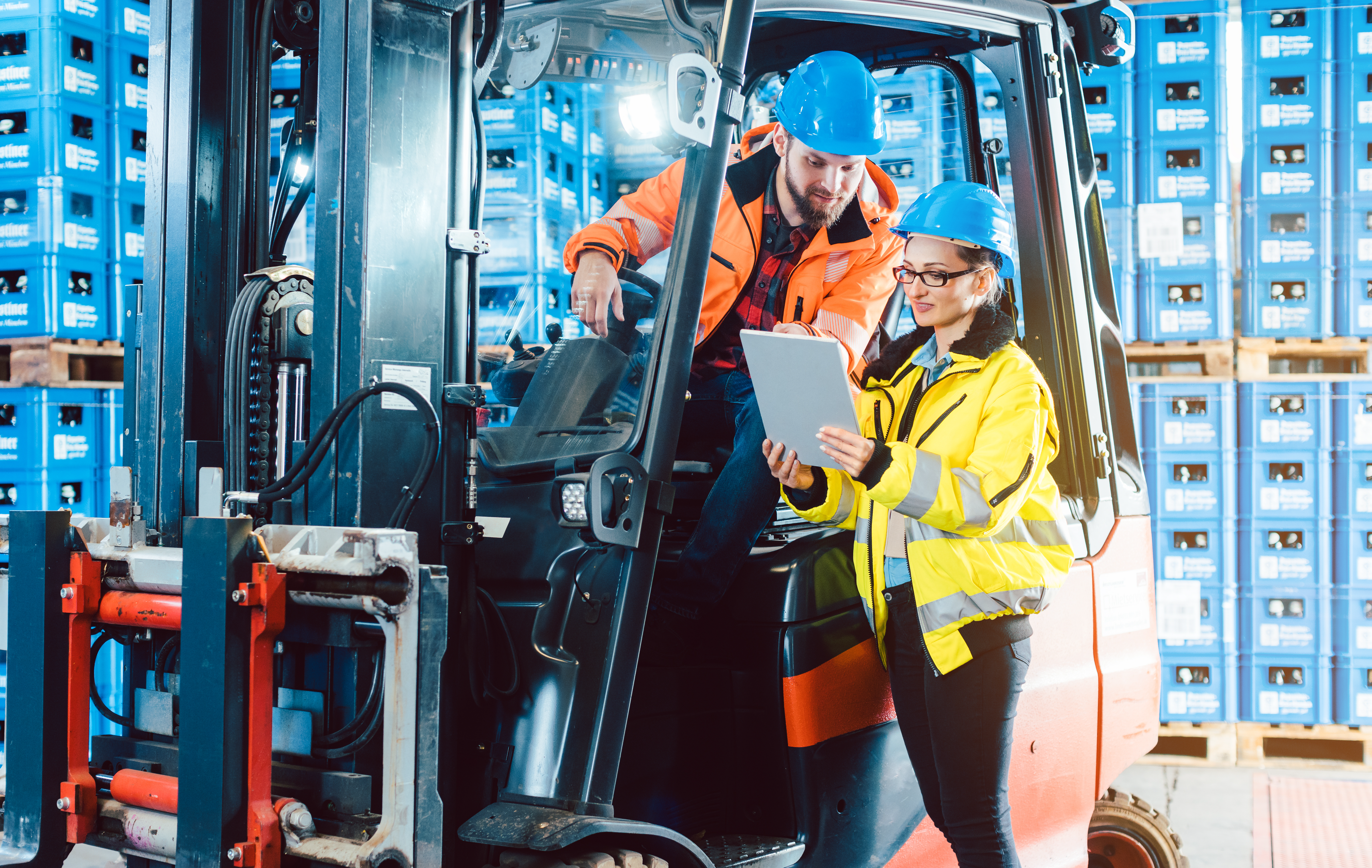 A female floor manager talking her colleague sitting on a forklifter.